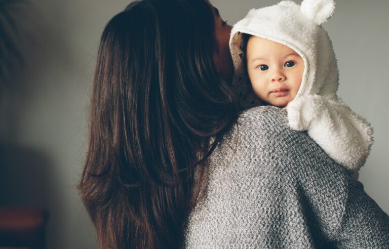 Mother holding young baby. baby is facing the camera, mothers head is turned away