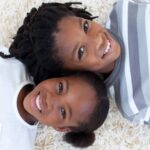 Two children aged 6 to 11 lying on the floor and smiling at the camera