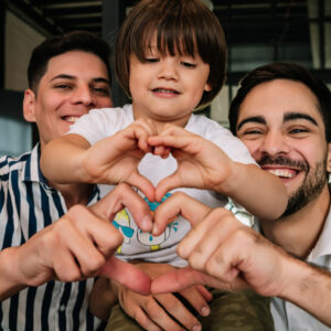 LGBTQ+ foster dads and foster child making hearts with fingers